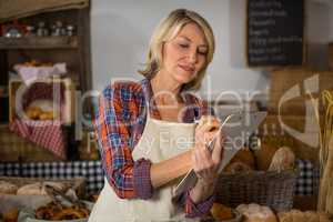 Smiling female staff writing on clipboard at bread counter