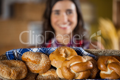 Smiling female staff holding wicker basket of various breads at counter