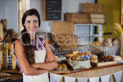 Portrait of smiling female staff standing with arms crossed at bakery shop