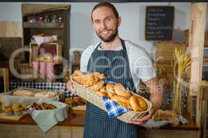 Smiling male staff holding wicker basket of various breads at counter