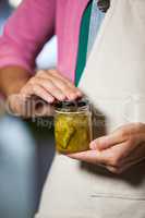 Shop assistant holding a jar of pickle in grocery shop