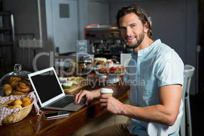 Smiling man having coffee while using laptop at counter