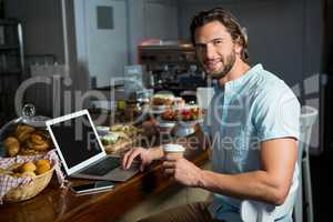 Smiling man having coffee while using laptop at counter