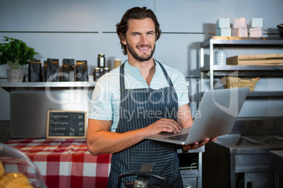 Smiling male staff using laptop at counter