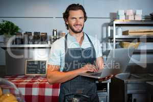 Smiling male staff using laptop at counter