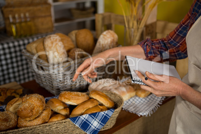 Female staff maintaining stock record at bread counter