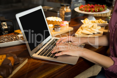 Woman using laptop at bakery counter in market