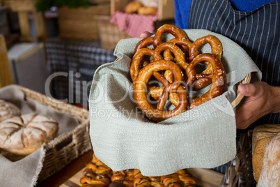 Mid section of staff holding wicker basket of pretzel breads at counter