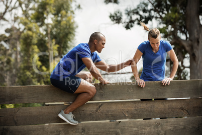 Male trainer assisting woman to climb a wooden wall