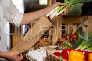 Staff packing spring onion in paper bag at grocery shop