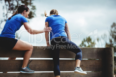 Female trainer assisting woman to climb a wooden wall