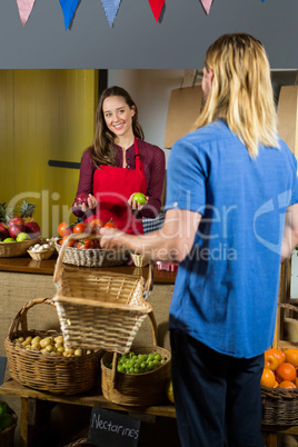 Smiling female staff offering fruits to customer at organic section