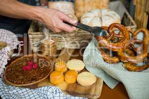 Staff holding pretzel with tong in bakery shop