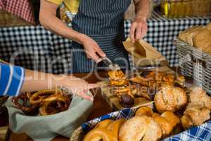 Mid section of staff packing sweet food in paper bag at counter