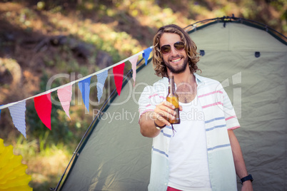 Portrait of man showing beer bottle at campsite