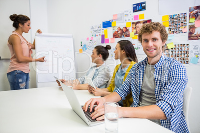 Portrait of executive using laptop while colleague discussing in background
