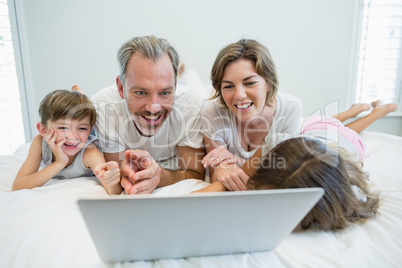 Smiling family using laptop on bed in bedroom