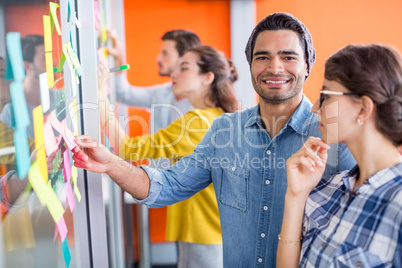 Portrait of smiling executives reading sticky notes on glass wall