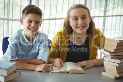 Smiling school kids reading books in library at school