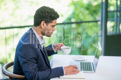 Businessman holding coffee cup while using laptop