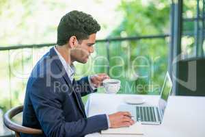 Businessman holding coffee cup while using laptop