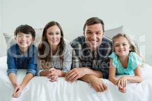 Portrait of smiling family lying on bed in bedroom