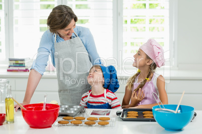 Smiling mother and kids interacting with each other while preparing cookies