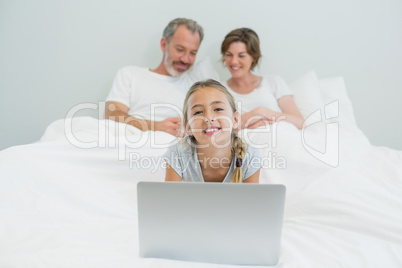 Portrait of smiling girl using laptop while parents resting in background