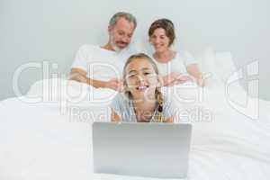 Portrait of smiling girl using laptop while parents resting in background