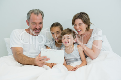 Family using digital tablet on bed in bedroom at home