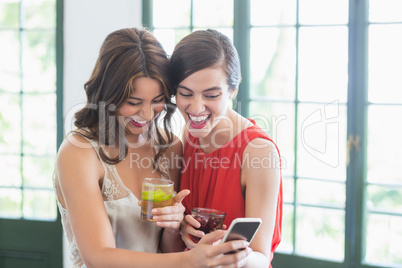 Friends with cocktail glasses while using mobile phone