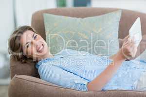 Happy woman using digital tablet while lying on sofa in living room