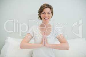 Smiling woman doing meditation on bed in bedroom at home