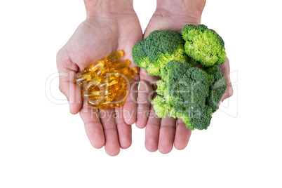 Close-up of hands holding broccoli and vitamin pills