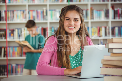 Portrait of happy schoolgirl using laptop in library