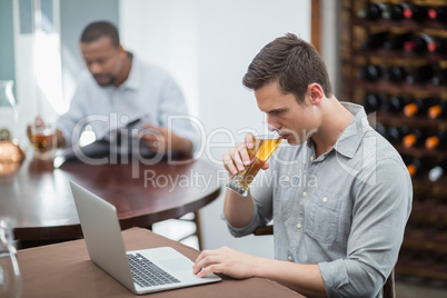 Handsome man drinking beer while using laptop