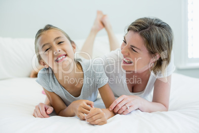 Smiling mother embracing her daughter while lying on bed in bedroom