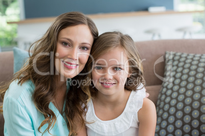 Smiling mother and daughter sitting on sofa in living room at home