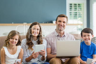 Smiling family using digital tablet, phone and laptop in living room at home