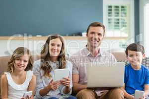 Smiling family using digital tablet, phone and laptop in living room at home
