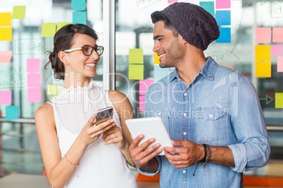 Smiling executives interacting with each other while using mobile phone and digital tablet