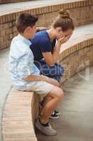 Schoolboy consoling her sad friend on steps in campus