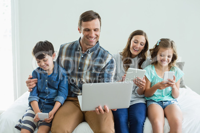 Smiling family using laptop, digital tablet and mobile phone in bedroom