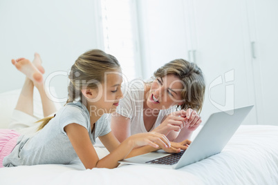Mother and daughter interacting with each other while using laptop on bed