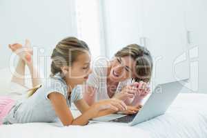 Mother and daughter interacting with each other while using laptop on bed