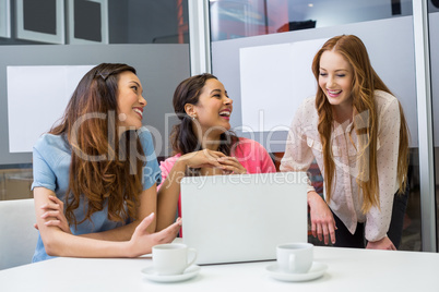 Smiling executives discussing over laptop in conference room