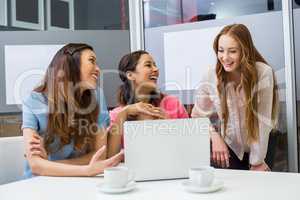 Smiling executives discussing over laptop in conference room