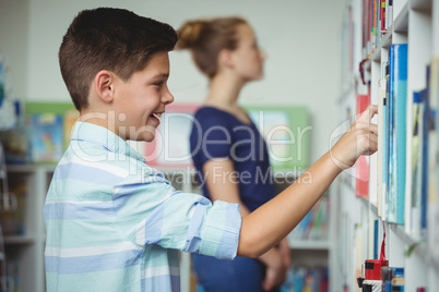 Schoolboy selecting book from book shelf in library