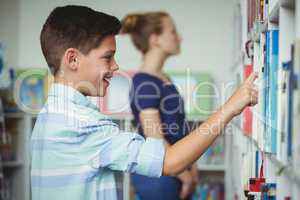 Schoolboy selecting book from book shelf in library