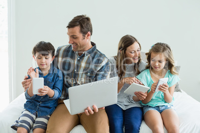 Smiling family using laptop, digital tablet and mobile phone in bedroom